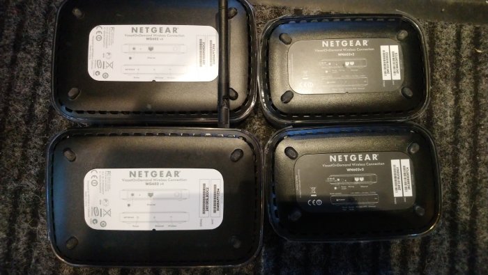 Fyra NETGEAR burkar placerade på bänk med baksidor uppvisande modell- och serienummer.