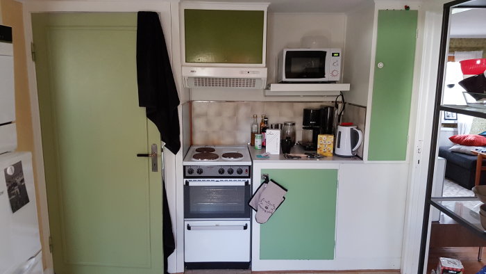 Ett litet kök i torp med spis, skåp och golv i vita och gröna nyanser, antyder pågående renovering.