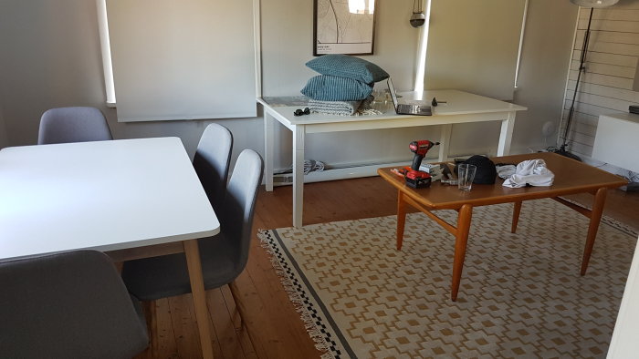 Ostilat vardagsrum med matbord, stolar, skrivbord och verktyg utspridda på golvet.