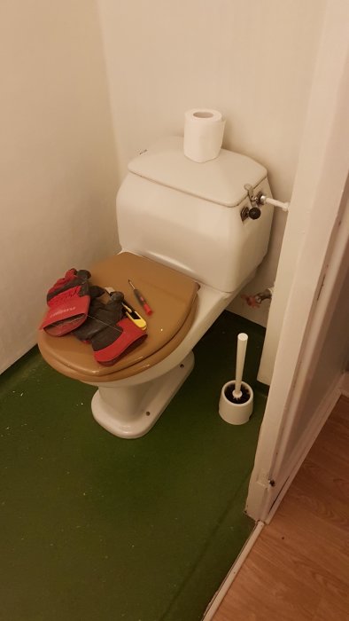 Toalett med verktyg och arbetshandskar på sitsen och en toalettpappersrulle på cisternen.