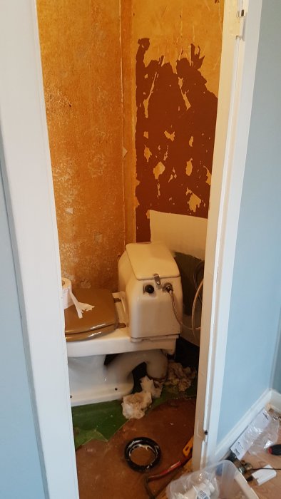 Ofärdigt badrum med en installerad toalett omgiven av byggmaterial och avskalad vägg.