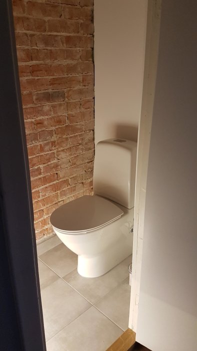 Nyinstallerad toalettstol i ett rum med synliga tegelväggar och kakelgolv.