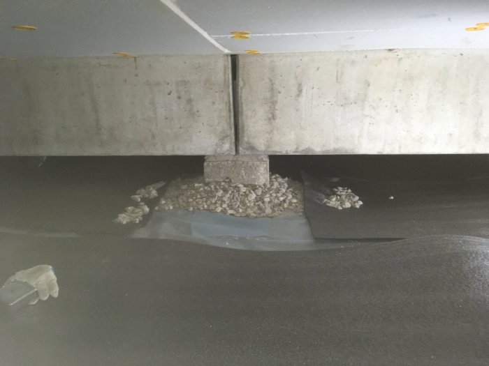 Concrete slab with exposed gravel and plumbing in foundation area, where a post is planned to stand, illustrated in a construction project context.