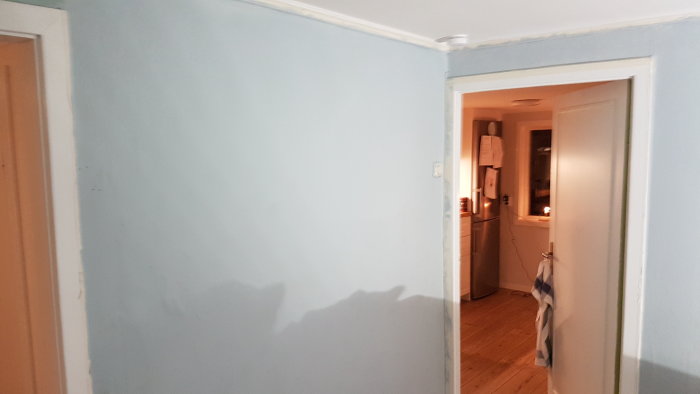 Vy över en tom korridor och öppen dörr till ett rum med trägolv och ljusa väggar som ska renoveras.