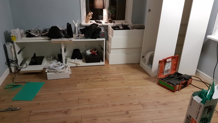 Sovrum under renovering med nytt trägolv och vit garderob, elverktyg och material spridda på golvet.