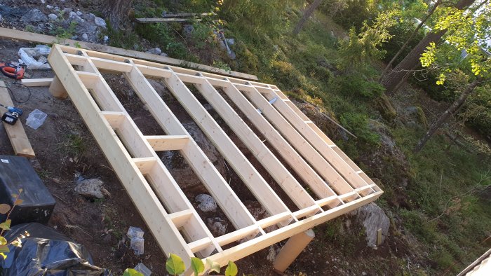 Grundram för byggprojekt med nedsänkt bjälklag i en skogsmiljö, verktyg och material syns.