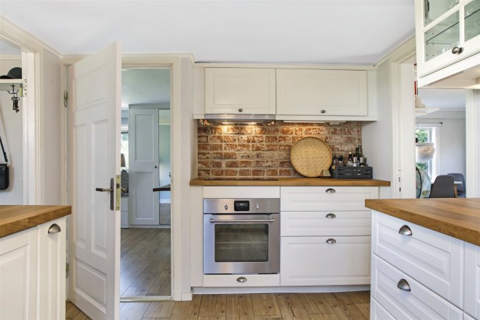 Stilfullt kök med vita skåp, träbänkskivor och en tegelvägg som stänkskydd.