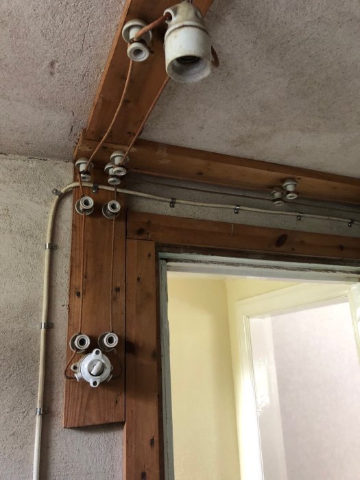 Gammal elinstallation med keramiska säkringar på en träpanel vid ett dörrfönster.