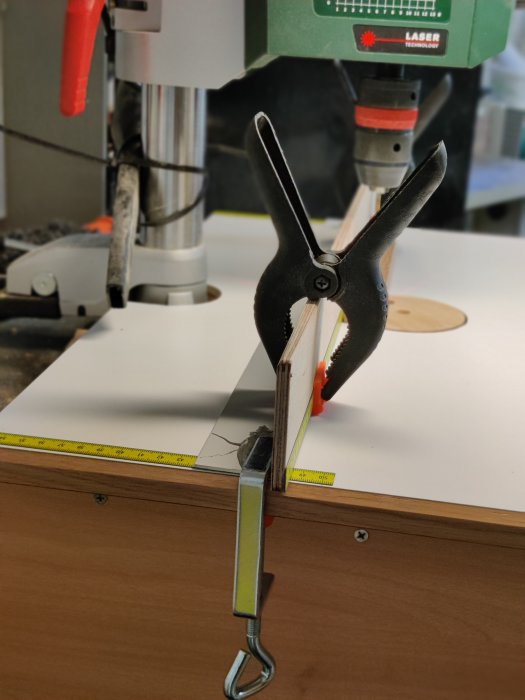 DIY bord med en laminerad kökslucka och aluminium vinkelprofil fäst med minitvingar och måttband nära borr.