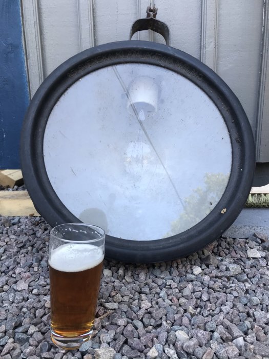 Gammal byggstrålkastare från Svenska Klamplampan Malmö står på grus, bredvid ett glas öl.