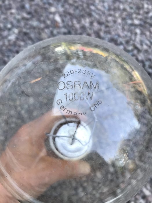 Närbild på en OSRAM 1000W glödlampa med specifikationer synliga genom smutsigt glas.