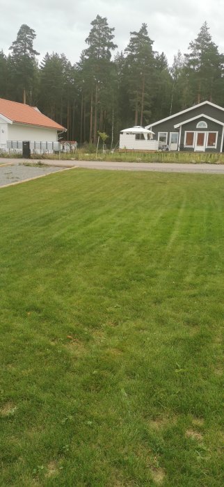 Välansat gräs med klara hjulspår från gräsklippare framför hus och husvagn.