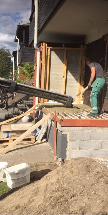 Person renoverar ingången till ett hus, häller betong nära trappa och byggmaterial ligger utspritt.