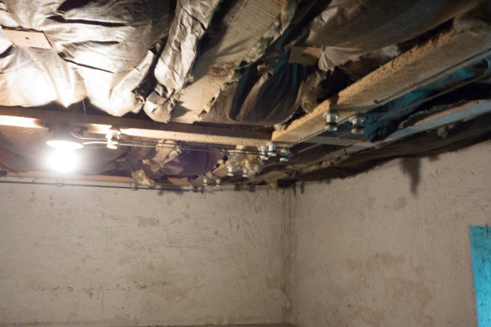Gamla isolerade takbjälkar och exponerade ledningar i en potatiskällare.