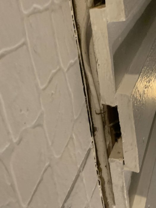Vit fasad med strukturerad yta och en synlig del av ett fönsterkarm i hörnet.