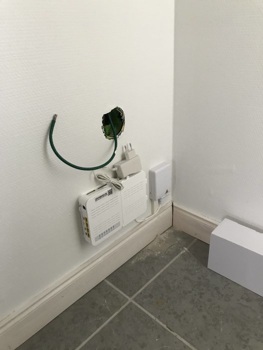 Nyligen installerad inomhusutrustning för grävarbete med en grön kabel som sticker ut ur en vägg och ett eluttag.