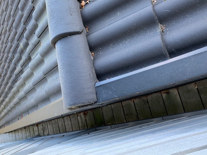 Nockpanna på tak avslutas tajt mot grå plåt med synligt urtag, vid en carport.