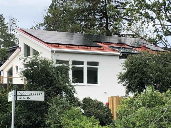 Hus med nyinstallerade solpaneler på taket omgivet av grönska.