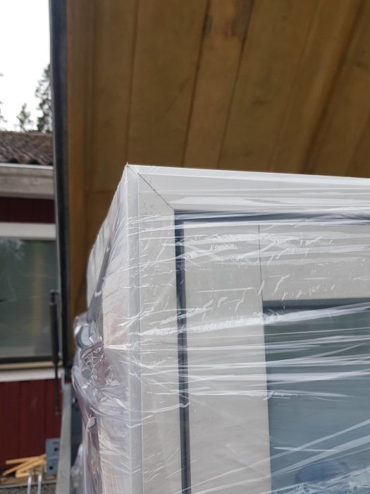 Närbild på ett inplastat fönster med alubeklädnad på utsidan vid en byggnad.