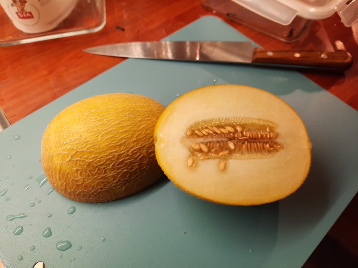 Halverad ananasmelon med frön på ett skärbräde bredvid en kniv.