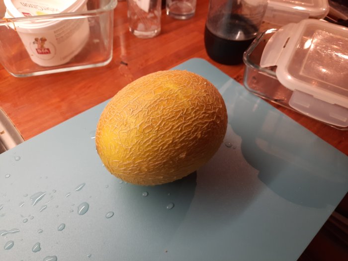 En nyskördad ananasmelon ligger på ett blått skärbräde med vattendroppar runt sig.