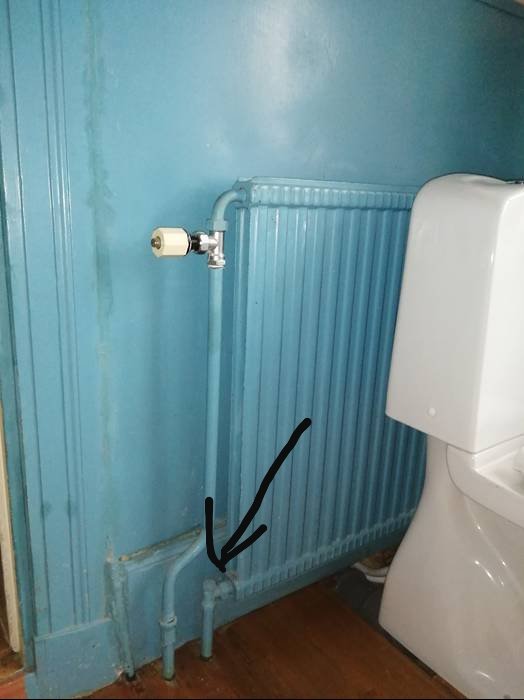 Radiator med avstängningsventil och markerad punkt för avstängning nära golv.