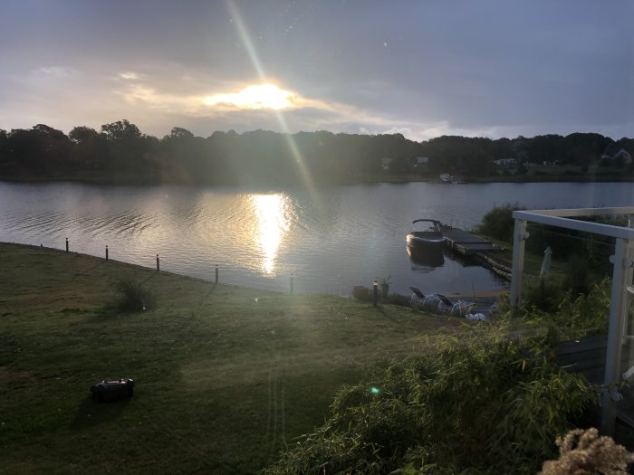 Soluppgång över ett mörkt landskap med reflektion i vattnet och en båt vid en brygga.