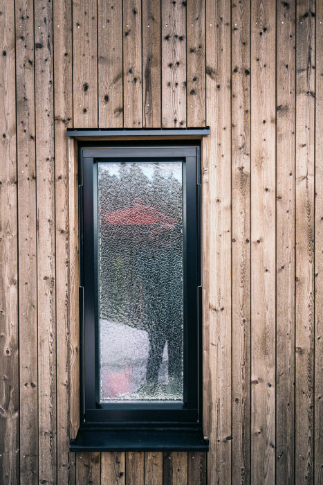 Vertikal spårpanel utan fasad kant på en vägg runt ett fönster med condens.