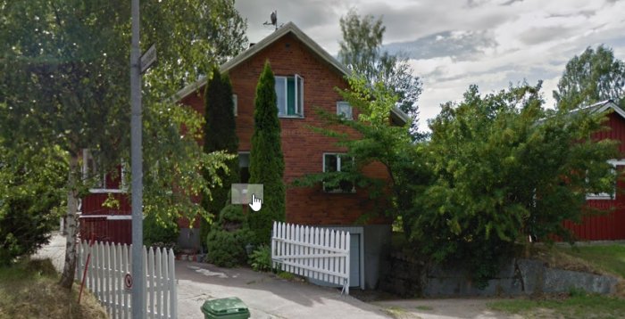 Tegelhus byggt 1909 på en slänt, med träd och garage, intill en cykelbana.