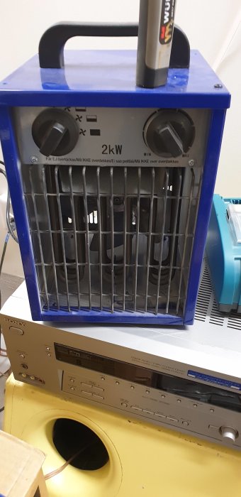 En blå byggtork med inställningsrattar ovanpå en gul högtalare och elektronisk utrustning.