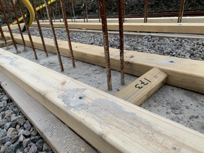 Grund för byggprojekt med träreglar fästa i betong och vertikala armeringsstänger som står i rad.