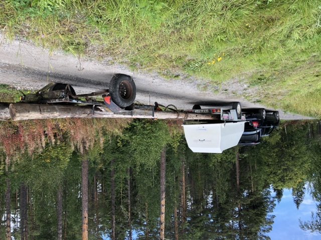 Kasserade telefonstolpar ligger på en släpvagn vid en skogsväg.