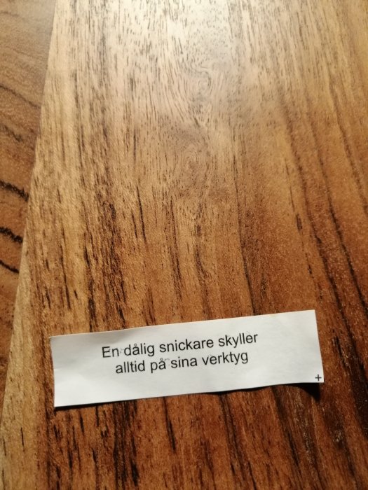 Lapp med texten "En dålig snickare skyller alltid på sina verktyg" på ett träbord.