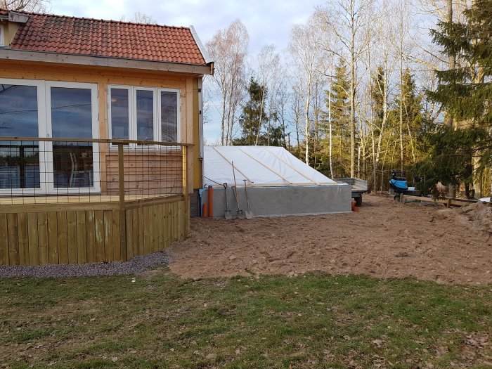 En altan i anslutning till ett hus med ett pågående byggprojekt och en täckt byggnad i bakgrunden.