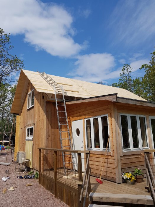 Renovering av gammal sommarstuga med nytt tak under konstruktion, träpanel och altan syns.