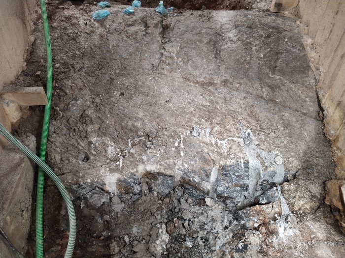 Bild av ett berggrundsklippe med synliga långa sprickor och en förekomst av svartglittrande mineral.