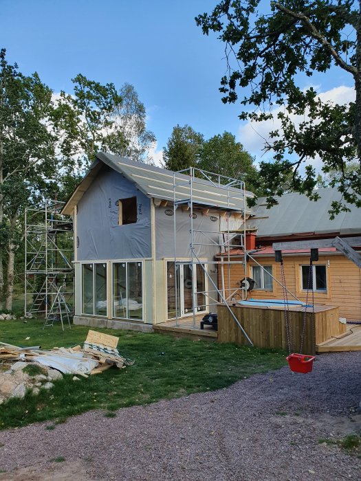 Hus under renovering med pågående isoleringsarbete, fasadskivor och byggställning syns.