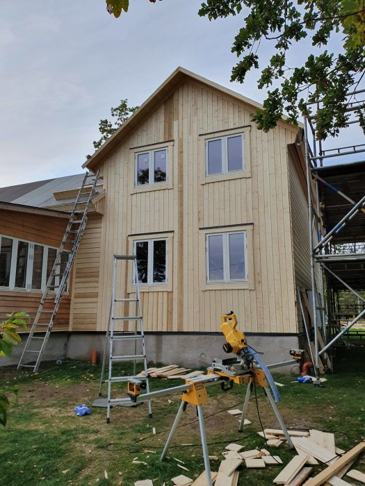 Nybyggt hus med liggande träfasadpanel och stående panel på gaveln, byggmaterial och verktyg framför.