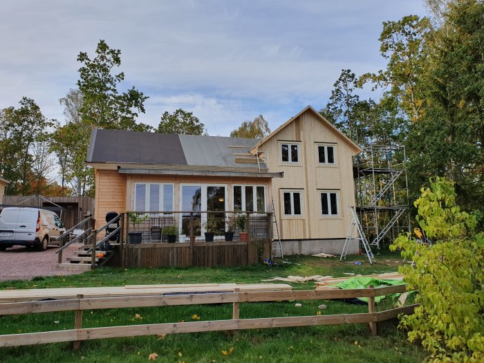 Hus under renovering med ny fasadpanel, liggande på sidan och stående på gaveln, omgiven av byggnadsställning.