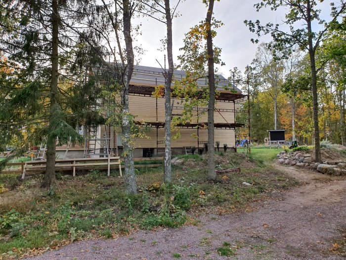 Hus under renovering med ny liggande fasadpanel på sidor och stående på gavel, omgiven av skog.