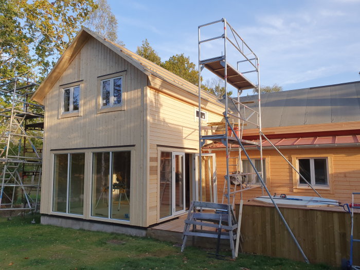 Ett hus under renovering med liggande träfasadpanel på sidorna och stående på gaveln, ställningar uppställda.