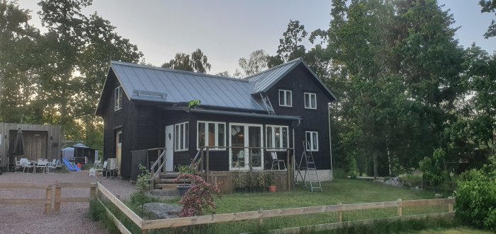 Renoverat trähus med svart brun trätjära på fasaden, blå himmel och omgivande grönska.