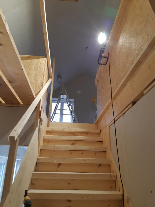 Trätrappa i ett hem under renovering med gipsväggar och OSB-skivor innan slutlig inredning.