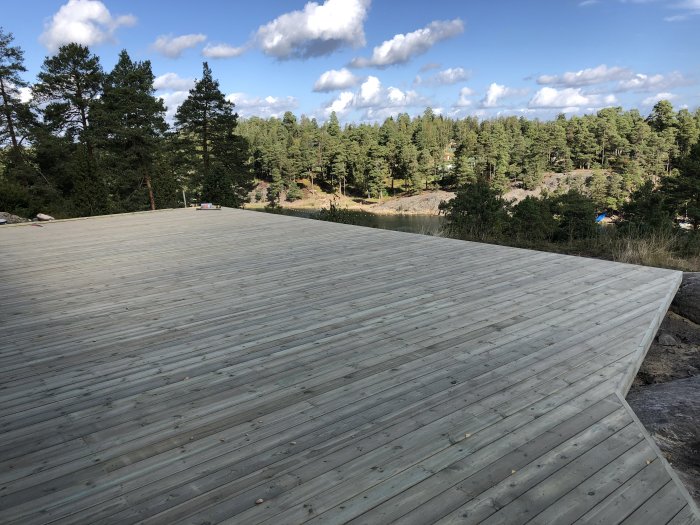 Stor träterrass med utsikt över skog och klar himmel, meddelar att bygget är stabilt.