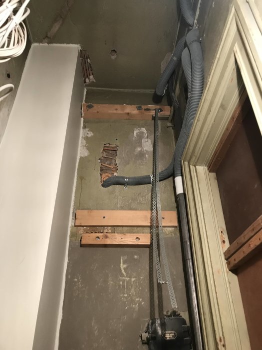 Omfärdigad installation av klinkergolv med synliga rör och oavslutade väggar i ett förråd omdanat till badrum.