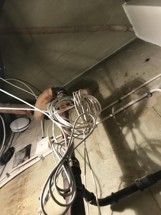 Oorganiserade elkablar och rör mot en grov och oavslutad vägg i ett renoveringsprojekt.