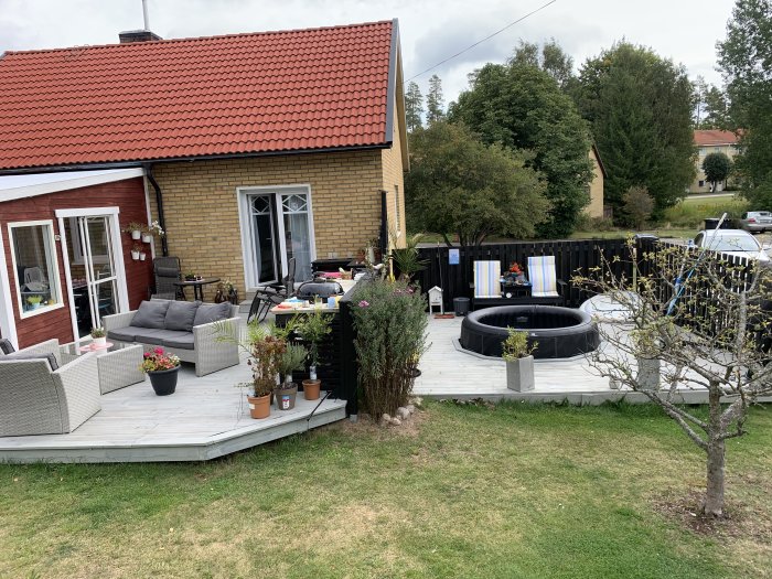 Gammalt trädäck vid ett gult hus med utemöbler och en rund pool, omgiven av en svart staket.
