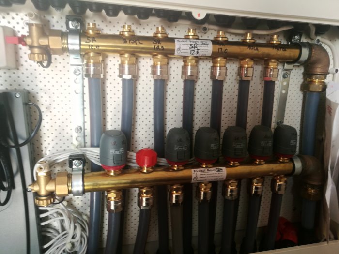 Installation av Roth golvvärme med fördelare och termostatventiler på en vägg, verktyg synliga.