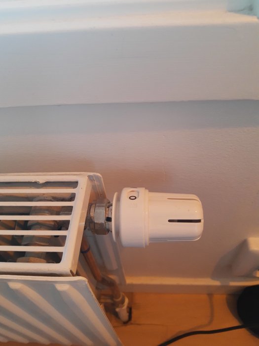 Termostat på radiator som visar tecken på läckage nära golvet.