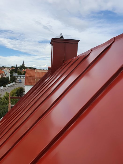 Nyinstallerad röd plåttak med skorsten och utsikt över stadsbebyggelse i bakgrunden.